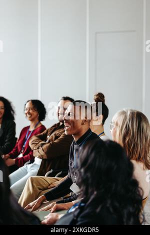 Uomo d'affari che ride in un seminario con un gruppo di persone diverse. Atmosfera positiva e interazione gioiosa durante una riunione d'affari. Foto Stock