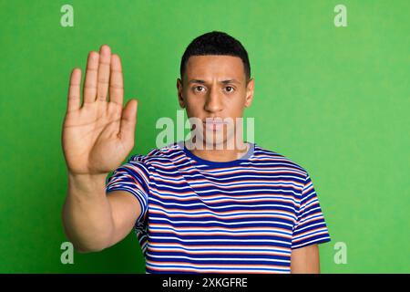 Ritratto di un bravo giovane braccio mostra abbastanza STOP indossare t-shirt isolata su sfondo di colore verde Foto Stock