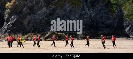 Un'immagine panoramica di un gruppo di vacanzieri maschi che giocano a giochi per riscaldarsi prima di una lezione di surf con il Newquay Activity Centre su GT Great Western B. Foto Stock