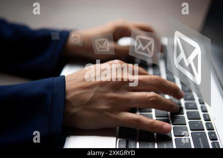 Primo piano di una mano che digita sulla tastiera di un notebook con diverse icone di posta elettronica mobili. Concetto di invio e ricezione di e-mail. Foto Stock