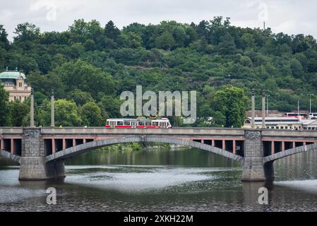 Tram rosso d'epoca retrò passando per un ponte sul fiume Moldava, mezzi di trasporto pubblici per le strade di Praga, capitale della Repubblica Ceca, il 3 luglio 2024 Foto Stock