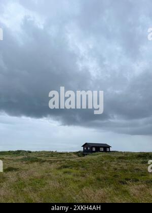 Danimarca, Skagen - 8 luglio 2024: Due turisti che si recano in una casa solitaria e pittoresca in stile danese su un prato sotto il cielo nuvoloso e scuro prima di piovere Foto Stock