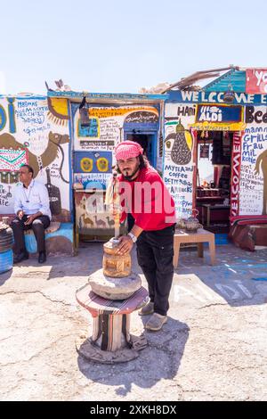 Il proprietario macina il caffè in un macinacaffè tradizionale presso la caffetteria Aldi Bedouin e un chiosco di souvenir presso il Moujib Panorama vicino a Wadi Mujib, in Giordania Foto Stock
