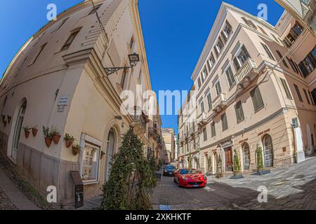 ALGHERO, ITALIA - 4 LUGLIO 2024: Moderni bolidi sulla stretta e tipica strada sarda, Piazza Civica, con l'edificio di Palazzo Bolasco all'incrocio Foto Stock