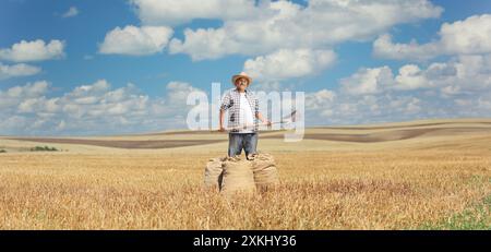 Agricoltore con una vanga e sacchi di bavaglio in un campo di grano Foto Stock