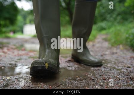 Donna con stivali di gomma verdi che cammina su una strada fangosa, primo piano Foto Stock