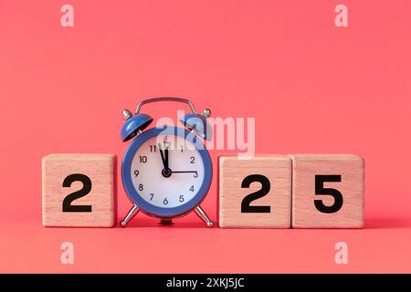 Anno 2025, felice anno nuovo. Blocchi di legno e un orologio che mostra l'anno prossimo. Bellissimo sfondo pesca Foto Stock