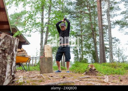 Uomo con ascia pesante. Ascia nel tagliafuoco tagliando a mano o tagliando tronchi di legno per l'inverno, la raccolta di legna da ardere in campagna Foto Stock