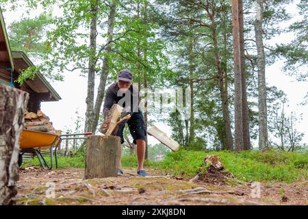 Uomo con ascia pesante. Ascia nel tagliafuoco tagliando a mano o tagliando tronchi di legno per l'inverno, la raccolta di legna da ardere in campagna Foto Stock