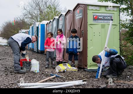 Servizi igienici e servizi igienici nella giungla gli operai installano servizi igienici e servizi igienici, sorvegliati da bambini migranti curiosi, diretti verso il Regno Unito. Dunkerque, Francia. Duinkerken The Jungle Nord Pas de Calais Francia Copyright: XGuidoxKoppesxPhotox Foto Stock