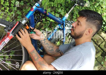 Un'immagine dinamica che cattura un giovane tatuato mentre sblocca la sua vecchia bici. Perfetto per temi legati alla vita urbana, al ciclismo e allo stile personale Foto Stock