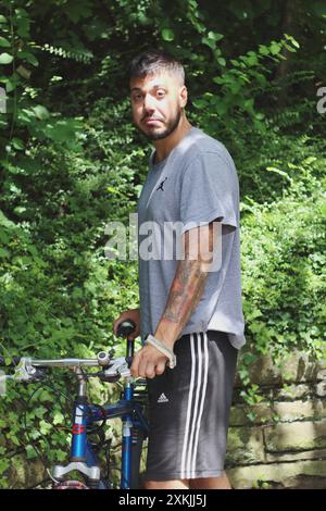 Un'immagine dinamica che cattura un giovane tatuato mentre sblocca la sua vecchia bici. Perfetto per temi legati alla vita urbana, al ciclismo e allo stile personale Foto Stock