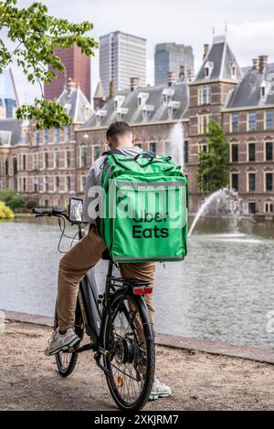 Servizio di consegna Uber Eats, autista addetto alla consegna che fa una pausa, presso la storica Binnenhof, sede del governo olandese, lo stagno Hofvijver, lo skyline del ci Foto Stock