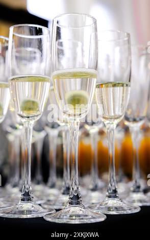 Diversi flute di champagne riempiti di champagne frizzante, ordinatamente disposti in file, pronti per una celebrazione formale. Scatto verticale. Foto Stock