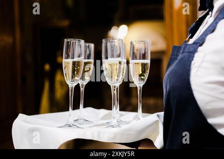 Cameriere in uniforme che serve flute di champagne su un vassoio con un panno bianco. Ripresa orizzontale. Foto Stock