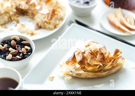 Dessert di mele, torta di pasta fila su un piatto bianco quadrato con una tazza di tè e noci su uno sfondo chiaro. Foto di alta qualità Foto Stock