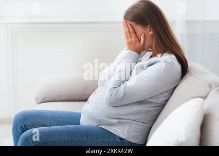 Donna incinta pianto che ricopre la faccia con le mani seduti a casa Foto Stock