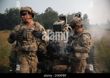 Cale Wood, un membro dell'equipaggio dei cannoni assegnato alla batteria A, 1st Battalion, 194th Field Artillery Regiment, 2nd Brigade Combat Team, 34th Infantry Division, Iowa Army National Guard, si gira per ricevere un altro round di artiglieria durante un'esercitazione di fuoco vivo con un obice M119A3 a Camp Ripley, Minn. durante una rotazione Exportable Combat Training Capabilities (XCTC) il 22 luglio 2024. Come membro dell'equipaggio dei cannoni, le sue responsabilità includono il funzionamento e la manutenzione delle attrezzature di artiglieria, il caricamento e il fuoco degli obici e l'esecuzione di missioni di fuoco. (Foto della Guardia Nazionale dell'Esercito degli Stati Uniti di SPC. Armani Wilson) Foto Stock