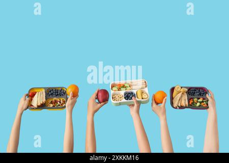 Mani femminili con cestini per pranzo scolastici e frutta su sfondo blu Foto Stock