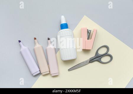 Flacone di colla, graffatrice e forbici su sfondo grigio. Vista dall'alto Foto Stock