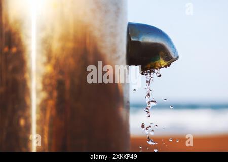 L'acqua sta cadendo da un rubinetto sulla spiaggia. Il tubo metallico gocciola d'acqua Foto Stock