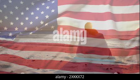 Immagine della bandiera americana su una coppia felice e variegata avvolta da un tappeto che abbraccia seduto sulla spiaggia del tramonto Foto Stock