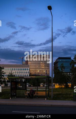 31.05.2024, Polonia, Wielkopolska, Poznan - uomo in attesa alla fermata dell'autobus Poznan Glowny (stazione ferroviaria principale), dietro di lui edifici di uffici di fronte a Foto Stock