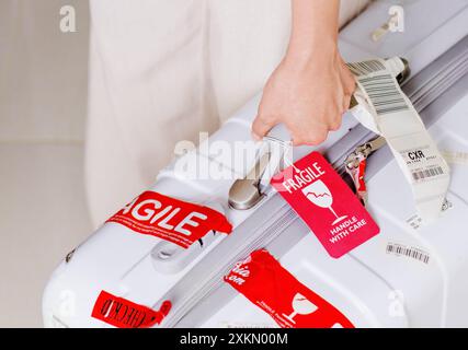 Uomo in possesso di valigia con targhetta rossa per bagagli (fragile) all'aeroporto Foto Stock