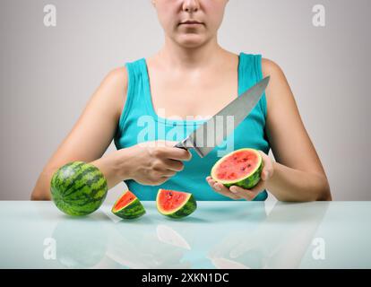 Ragazza che usa un grande coltello per tagliare piccoli angurie rosse mature Foto Stock