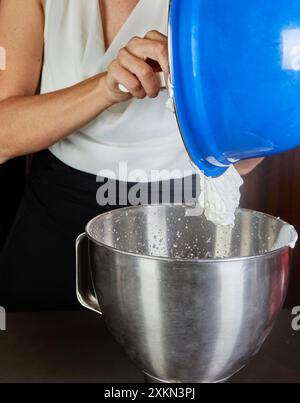 Donna che prepara il dessert tiramisù in una ciotola di metallo con una ciotola a lato nella cucina di casa. Ricetta passo passo. Foto Stock