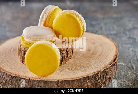 Macaron colorati gialli e bianchi su un supporto in legno su uno sfondo in cemento. Foto Stock