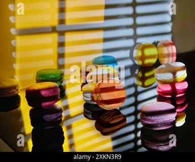 Un assortimento di macaron luminosi di diversi colori viene visualizzato su una superficie in vetro con uno sfondo decorativo astratto illuminato in pa diversi Foto Stock