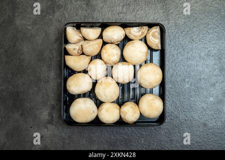 Un vassoio di funghi è seduto su un bancone. I funghi sono tagliati a metà e disposti in un quadrato Foto Stock