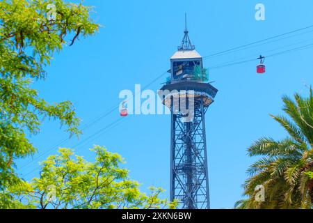 Barcellona, Spagna - 16 luglio 2024: Vista ravvicinata della torre della funivia del porto e delle cabine incorniciate da palme adagiate contro il vibrante cielo blu Foto Stock