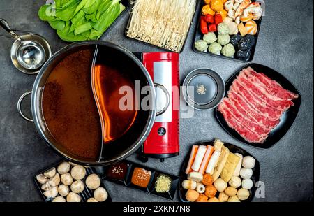 Una pentola rossa con coperchio si trova su un tavolo con una varietà di cibi, tra cui carne, verdure e salse. Il tavolo è pronto per un pasto, e il cibo l Foto Stock