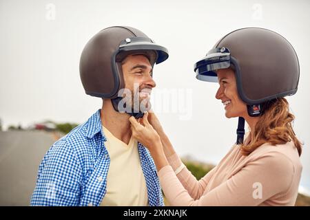 Coppia felice, casco e aiuto per il giro in moto, viaggio o avventura nella campagna d'Italia. Donna, uomo e sicurezza per partner, romanticismo o legame Foto Stock