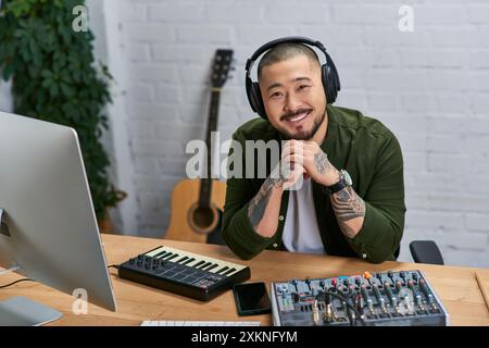 Un giovane asiatico in abbigliamento casual sorride mentre siede a una scrivania nel suo studio. Foto Stock