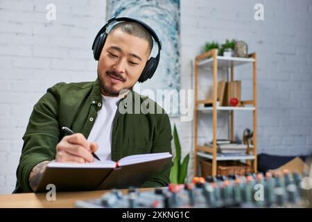 Un giovane asiatico in abbigliamento casual scrive su un notebook, indossando le cuffie in uno studio musicale. Foto Stock