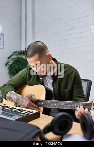 Un bell'asiatico, polistrumentista, suona una chitarra acustica nel suo studio. Foto Stock