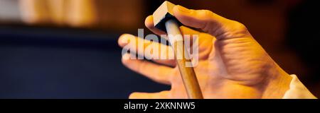 La mano di una persona tiene un segnale da biliardo, preparandosi a gesso prima di un colpo. Foto Stock