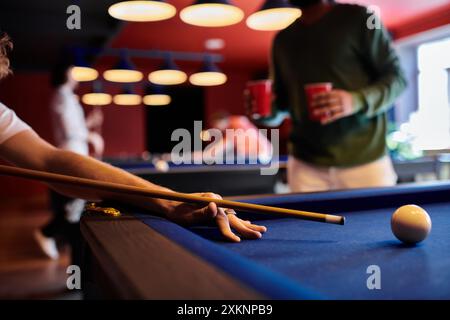 Un primo piano di un uomo che gioca a biliardo con gli amici in un ambiente informale. Foto Stock