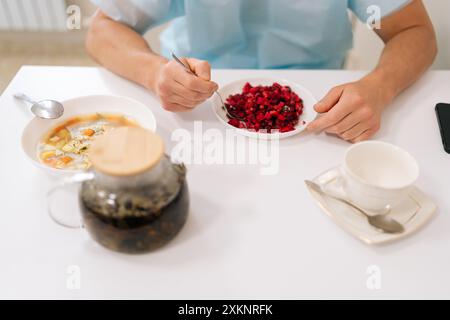 Vista dall'alto di paziente ospedaliero maschile irriconoscibile in giacenza di cappotto medico, mangiare prima operazione lunga in clinica. A un giovane piace mangiare seduto Foto Stock