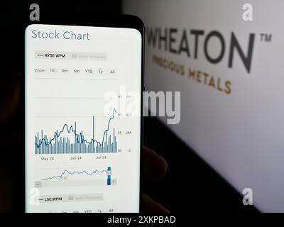 Persona che tiene un cellulare con pagina web della società canadese di metalli Wheaton Precious Metals Corp. Davanti al logo. Messa a fuoco al centro del display del telefono. Foto Stock