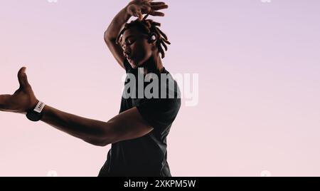 Ballerino maschile con movimenti espressivi e una vibrante energia danzano in uno studio. Indossa auricolari wireless, gli occhi chiusi, sentendo il ritmo. La Gen Z i. Foto Stock