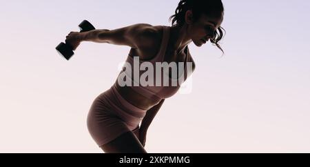 Una donna atletica solleva i pesi in uno studio, con particolare attenzione alla costruzione muscolare e all'allenamento di forza. Atleta femminile che utilizza manubri per un workou completo Foto Stock