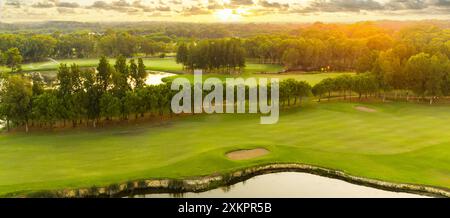 Panorama di uno splendido campo da golf al tramonto con un cielo spettacolare. Vista panoramica sul fairway del golf con laghetto. Campo da golf con splendidi pini Foto Stock