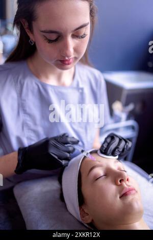 Iniezioni di bellezza. Una cosmetologa donna con guanti neri fa un'iniezione al suo cliente. Trattamento con acido ialuronico. Introduzione di liquido in Foto Stock