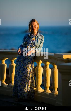 Una donna con un abito estivo leggero su una passeggiata fronte oceano al tramonto. Foto Stock