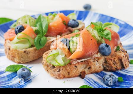 Colazione. Panini aperti con salmone salato, cetrioli e mirtilli. Specialità di pesce. Cibo sano. Foto Stock