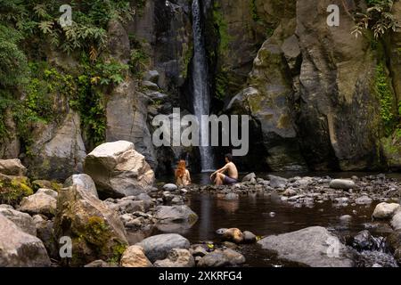 Coppia seduta davanti alla cascata di salto do Cabrito. Isola di Sao Miguel nelle Azzorre. Foto Stock